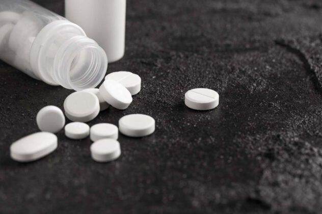 Weiße Tabletten liegen verstreut neben einer geöffneten weißen Plastikflasche auf dunklem Untergrund