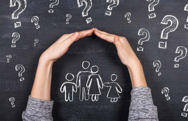 Zwei Hände formen ein Dach über einer Kreidezeichnung einer Familie auf einer Tafel mit Fragezeichen im Hintergrund