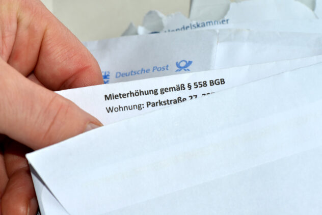 Hand zieht einen Brief mit dem sichtbaren Text 'Mieterhöhung gemäß § 558 BGB Wohnung: Parkstraße' aus einem weißen Umschlag mit dem Logo der Deutschen Post